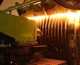 Induction hardening coil glowing orange against a machined drum during heat treatment