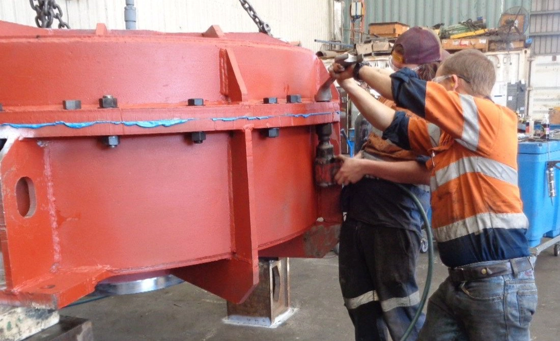 Two ABC fitters in hi-vis working on a large red-painted machinery casing assembly inside the workshop
