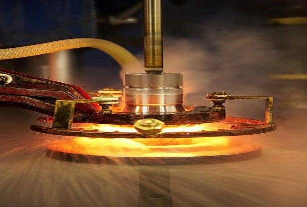 An induction-hardening coil glowing orange around a rotating steel component, heat haze rising