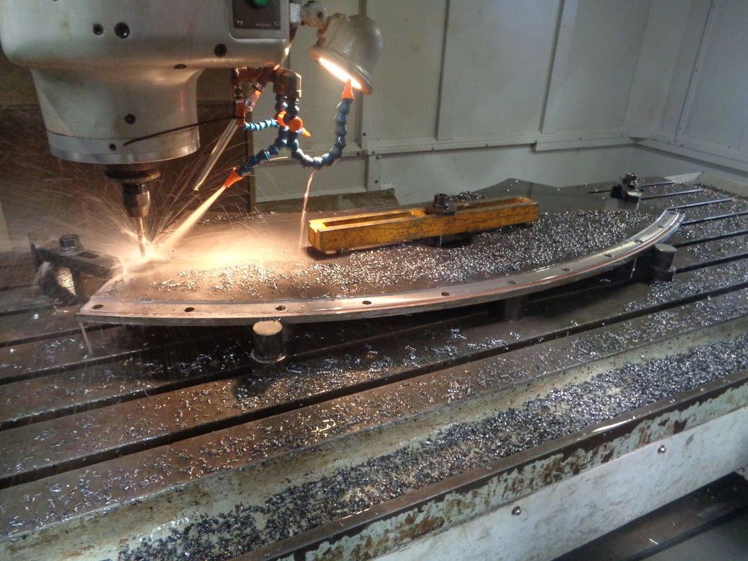 A CNC machine cutting a large curved steel arc segment clamped to the bed, swarf and sparks at the tool
