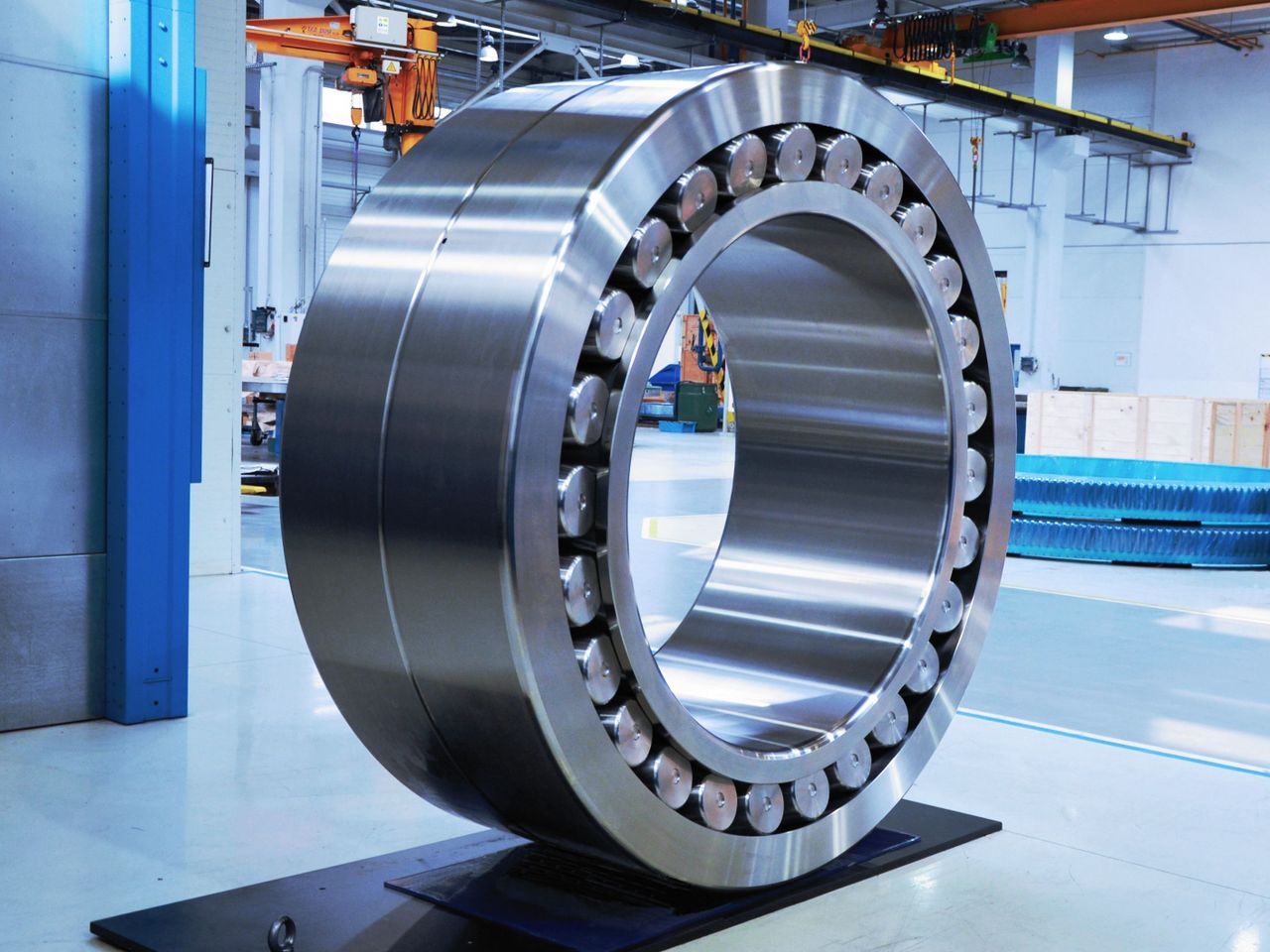 A large-diameter roller slew bearing, machined and polished, standing on a stand in the workshop