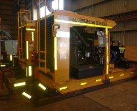 A skid-mounted dewatering pump unit with reflective striping inside the workshop