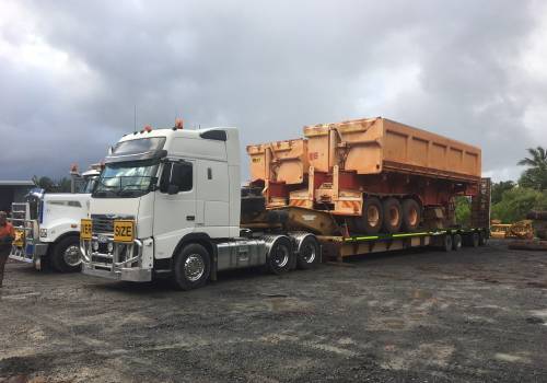 Tipper bodies stacked on an ABC low-loader in the yard under storm clouds