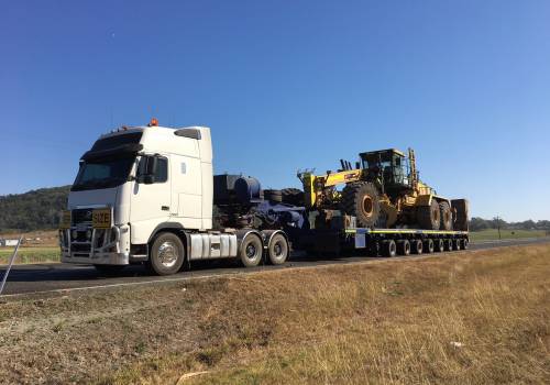 Mine-spec grader chained down on a multi-row low loader behind a prime mover on the highway