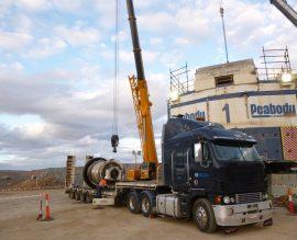 Mobile crane and prime mover with a large drum component on a flatbed at the base of a P&H mining shovel