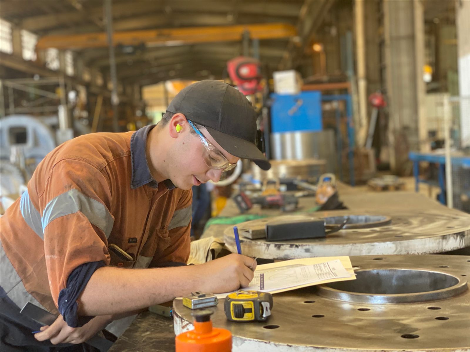 ABC tradesman in hi-vis recording QA measurements against a large machined flange in the workshop