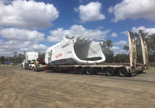 Oversize dragline bucket loaded on an ABC low-loader travelling a Queensland highway under blue sky