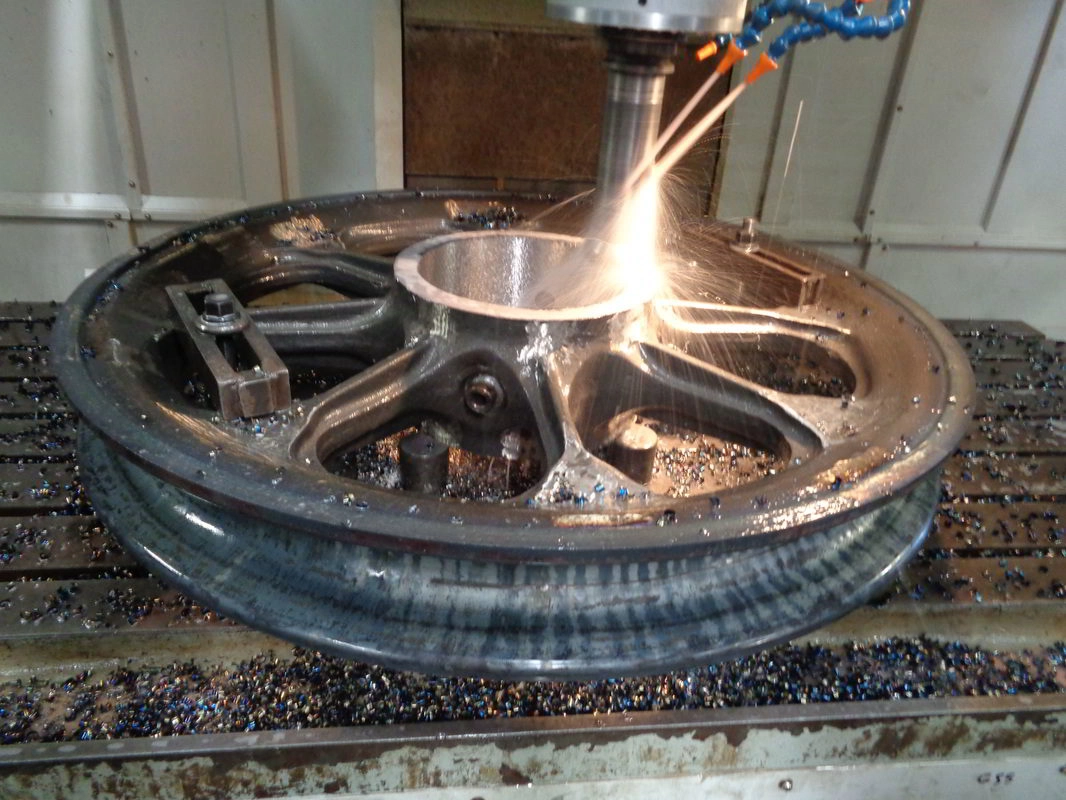 CNC milling cutter throwing sparks on a cast wheel component clamped to the machine bed
