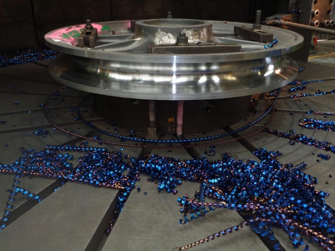 Mirror-finished sheave wheel on a vertical borer table, blue machining swarf scattered across the bed