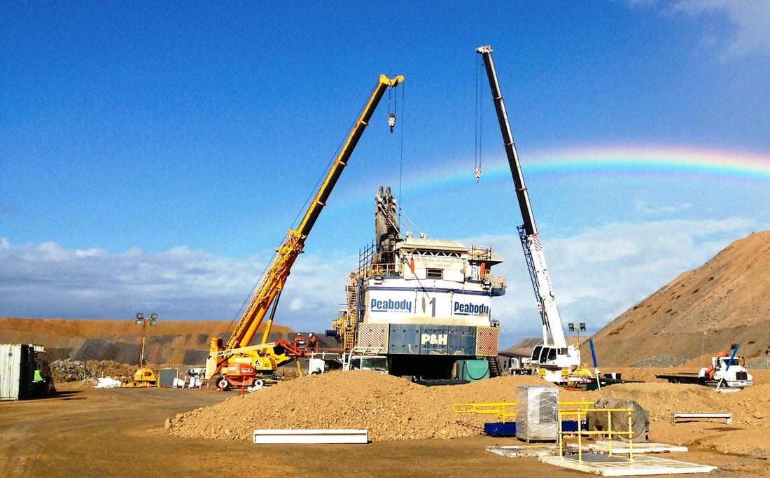 P&H face shovel being assembled between two cranes on a mine site, spoil piles behind