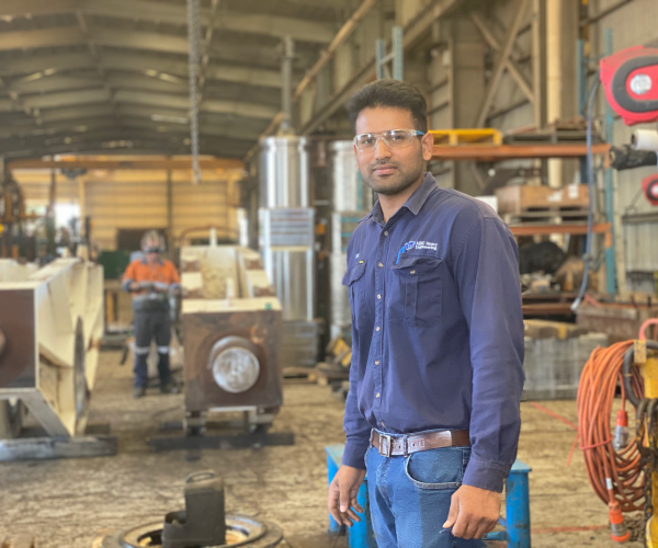 ABC engineer standing in the workshop with drawings prepared for laser cutting, machinery behind him